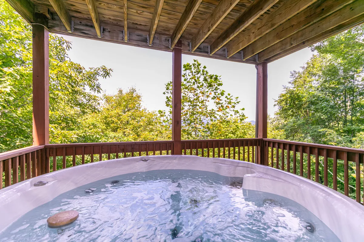 A serene scene featuring the hot tub set against a backdrop of greenery, inviting guests to unwind and savor the peaceful mountain environment. The hot tub is an ideal spot for relaxing after a day of exploration or enjoying intimate conversations under the stars.