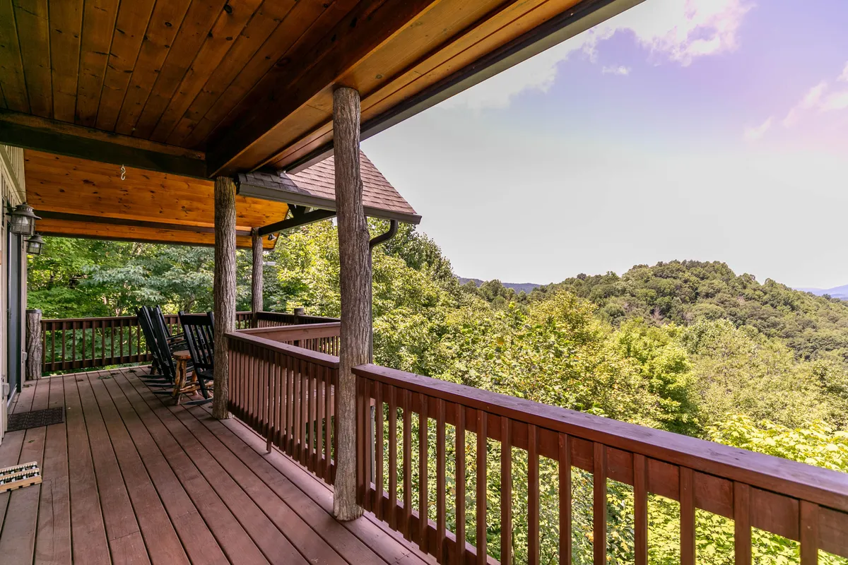 A tranquil porch scene with wooden rocking chairs facing a panoramic mountain view. The sturdy wooden railing frames the natural landscape, while the seating invites relaxation, wildlife spotting, or stargazing. The scene evokes peaceful moments after a day of adventure, reinforcing the mountain retreat atmosphere.