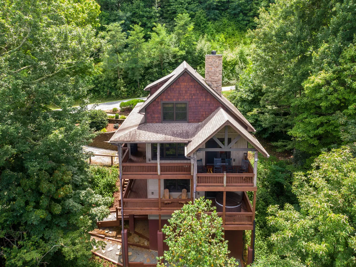 This image showcases the spacious wooden deck and stone chimney of Deer Moments, nestled among lush trees. The inviting deck offers ample room for groups to gather outdoors and connects seamlessly with the tranquil natural setting, embodying the cabin’s secluded mountain location.