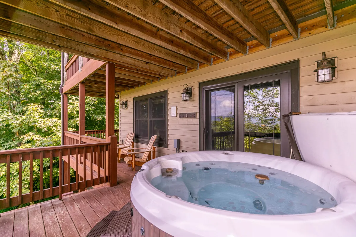 An inviting scene on a wooden deck featuring a bubbling hot tub surrounded by lush greenery. The deck offers a comfortable place to unwind while taking in nature views, perfect for post-adventure relaxation and evening stargazing.