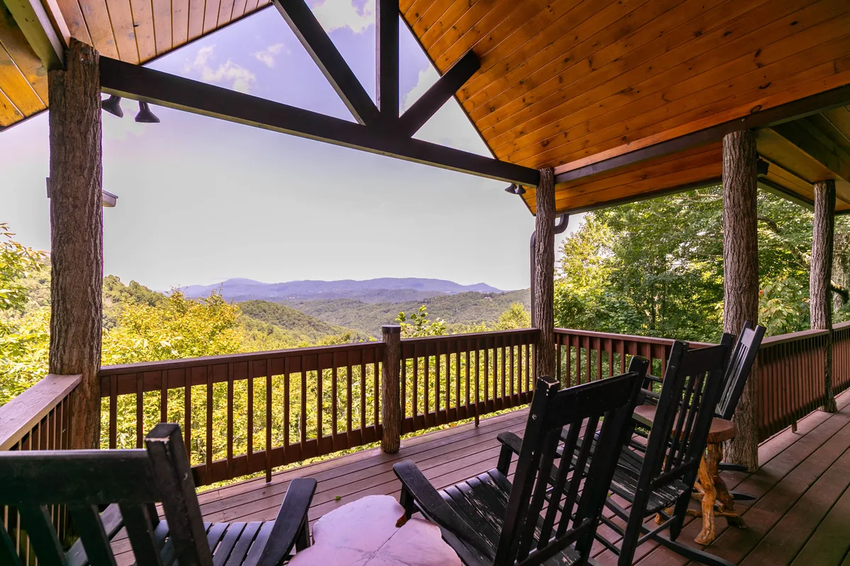 A peaceful exterior porch scene featuring rocking chairs positioned to overlook a sweeping mountain view. The wooden railing frames the view, and the setting is perfect for sunrise watching or stargazing, highlighting the peaceful comfort and connection with nature.