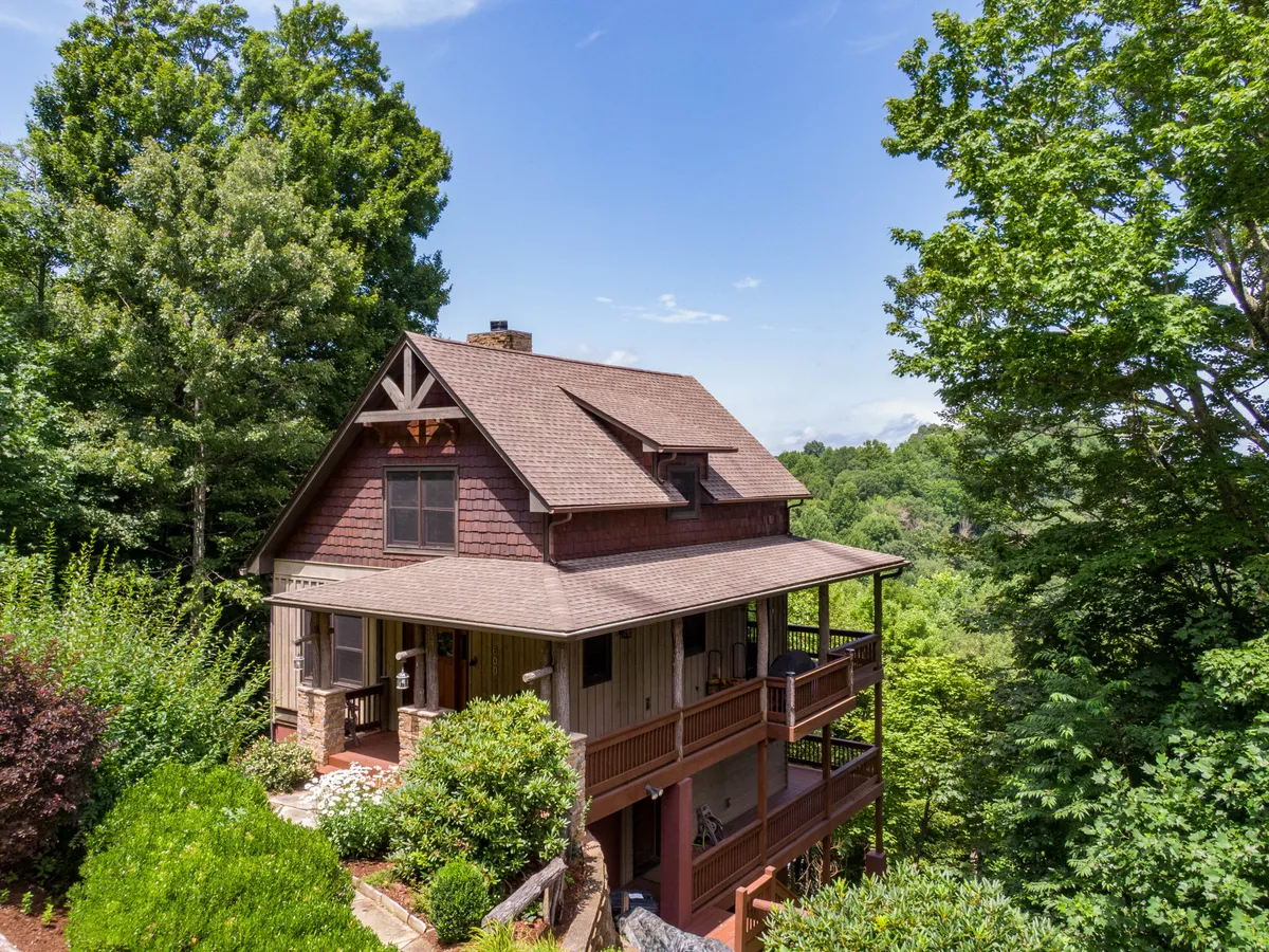 The house sits in a peaceful woodland setting, with a welcoming porch and surrounding trees, illustrating the seclusion and natural beauty of Deer Moments. The broad porch provides an inviting entrance and a space for outdoor gatherings, morning coffee, or evening chats.