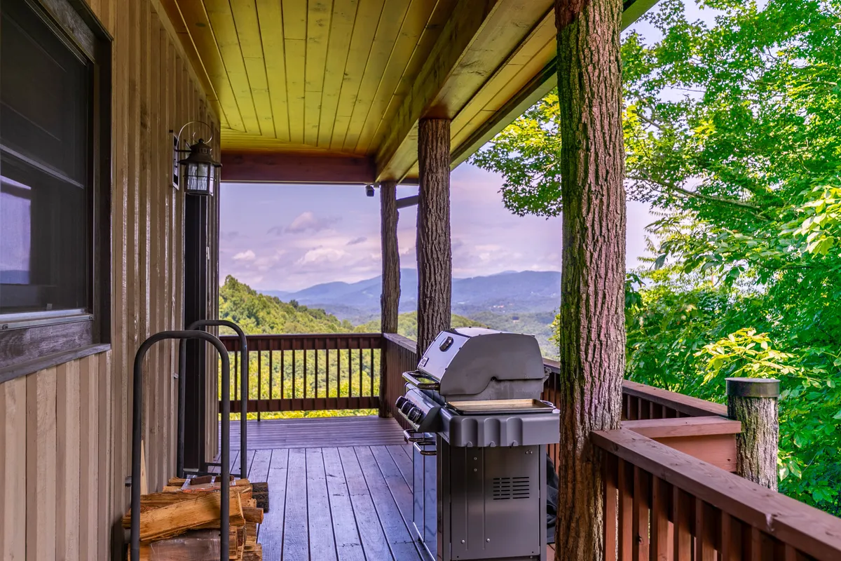 An outdoor grilling area on a wooden deck, complete with an infrared BBQ grill, wooden railing, and a scenic mountain backdrop. The setup is perfect for open-air feasts and social gatherings while taking in panoramic views.
