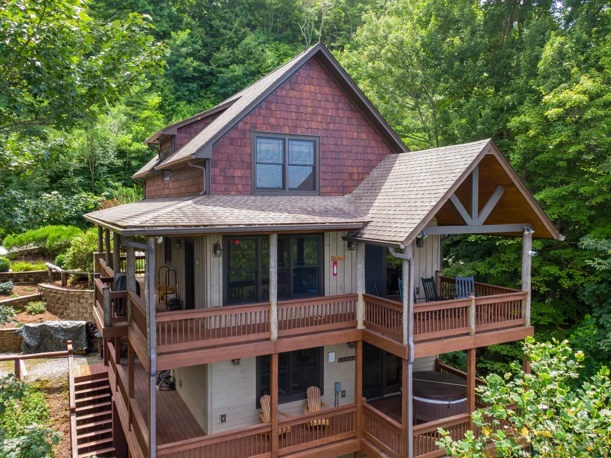 An exterior shot highlighting wooden balconies, lush greenery, and a hot tub tucked by the deck. The image conveys both the elevated structure of the home and the inviting outdoor amenities designed for relaxation and gathering with loved ones.